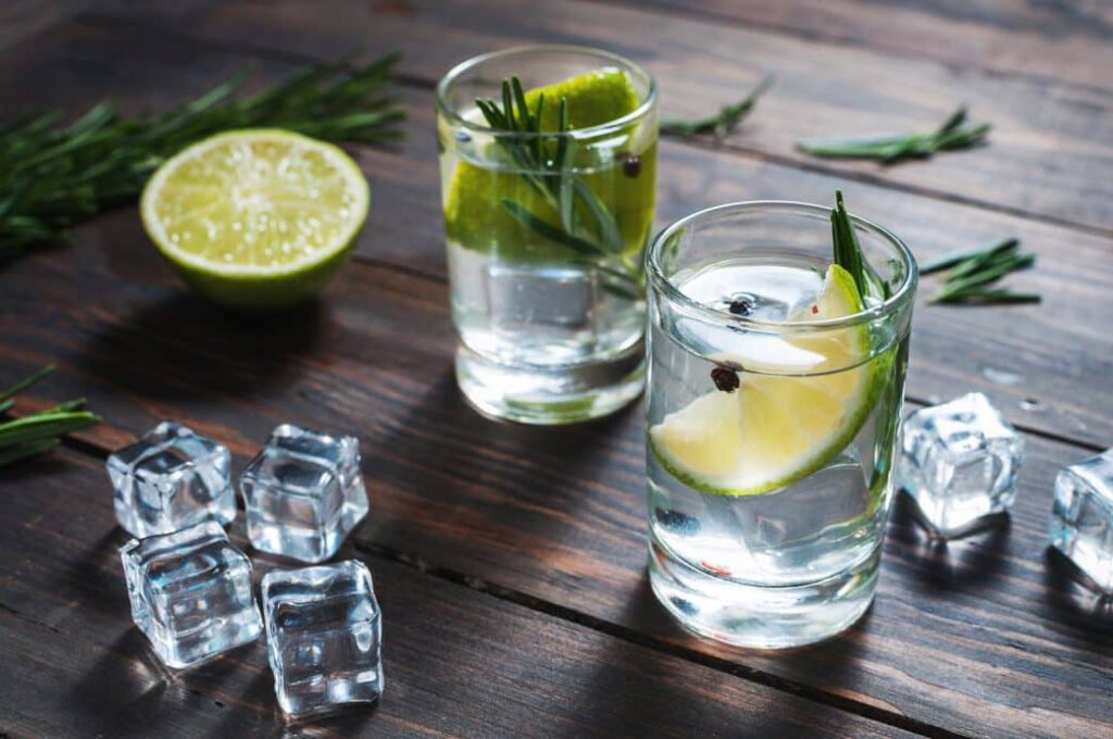 Shot glasses of alcohol with rosemary and lime